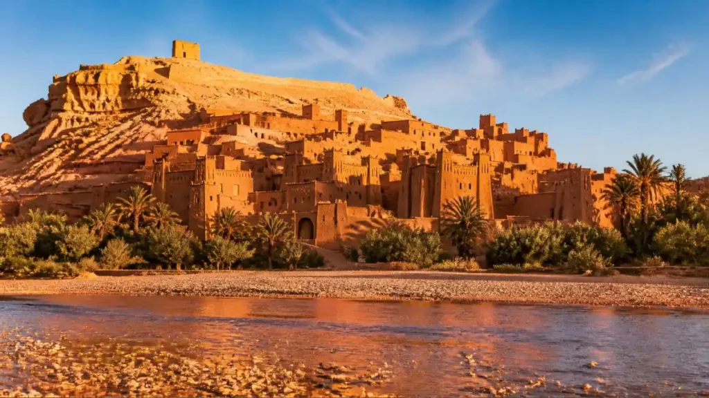 Aït Benhaddou kasbah rising above a riverbed and palm trees at sunrise