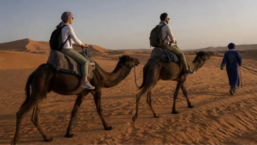 Travelers riding camels at sunset in the Erg Chebbi dunes near Merzouga.