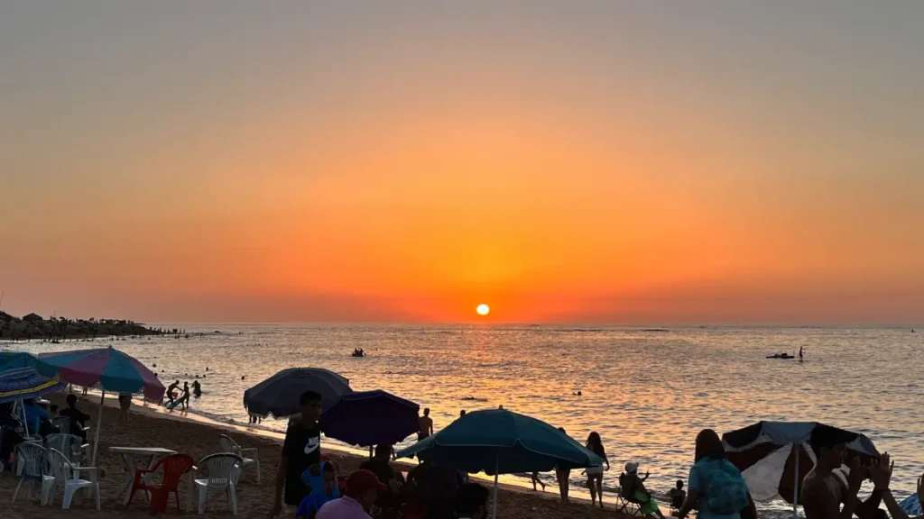 Sunset over Bouznika Beach with swimmers and umbrellas